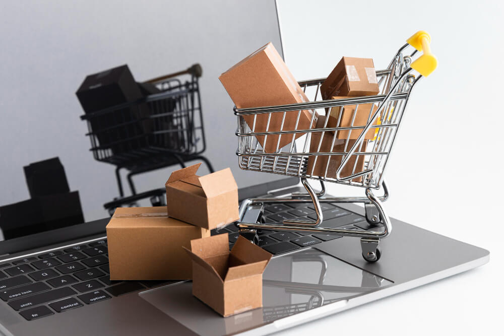 Carrito de compras con cajas sobre una laptop, representando compras en línea y comercio electrónico